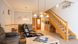 A modern living room with a sofa, a dining table, a chair, a staircase, and a kitchen area.