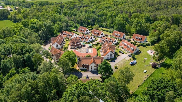 Luchtbeeld van een woongebied met huizen, omringd door weelderige begroeiing en een waterpartij op de achtergrond.