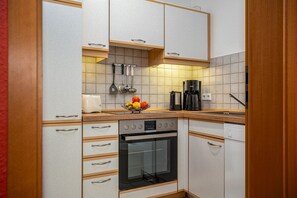 Una cocina compacta con horno integrado, cafetera y frutero sobre la encimera.