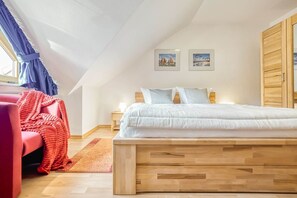 A bedroom with a wooden bed, a red chair, a nightstand, and two framed pictures on the wall. - Spacious terraced house in vacation park with terrace & communal pool - (Zingst)