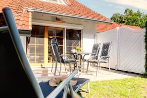 Een terras buiten met een tafel en stoelen, een overdekt gedeelte en een witte schutting.