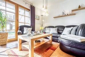A modern living room with a sofa, a coffee table, and a large window. - Spacious terraced house in vacation park with terrace & communal pool - (Zingst)