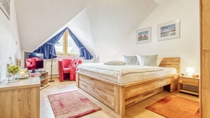 Ett sovrum med ett sluttande tak, en säng med en trägavel, ett skrivbord med en dator, en stol och ett fönster med blå gardiner.