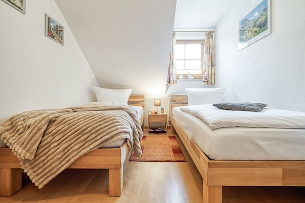 Een slaapkamer met twee bedden, een raam met gordijnen en een klein nachtkastje met een lamp.