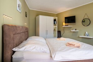 Une chambre d’hôtel comprenant un lit, une armoire, une télévision et une table de chevet avec une lampe.
