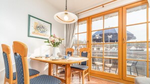 Un coin repas avec une table et des chaises en bois, un vase rempli de fleurs et, à travers une porte vitrée, une vue sur l’extérieur.