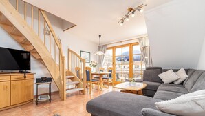 Un salon moderne avec un canapé gris, un escalier en bois et un coin repas comprenant une table et des chaises.