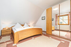 A bedroom with a wooden bed, a nightstand, a mirror, and a window with curtains. - Comfortable vacation apartment in a vacation park with balcony and pool in Zingst - (Zingst)
