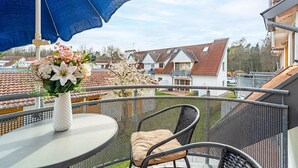 Un balcon avec une table ronde, une chaise, un parasol bleu et un vase de fleurs.