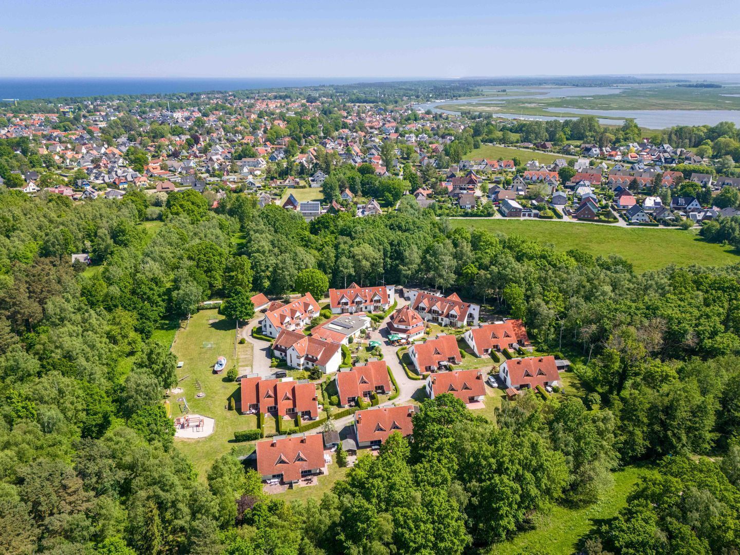 Vista aérea de una zona residencial con casas, áreas verdes y una masa de agua al fondo.