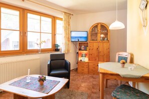 Um quarto aconchegante com uma mesa de madeira, uma cadeira preta, uma televisão e um armário com portas de vidro.