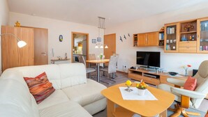 Ein modernes Wohnzimmer mit einer Couch, einem Esstisch, einem Fernseher und einem Bücherregal.