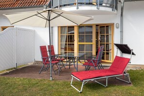 An outdoor patio with a table and chairs, a sun umbrella, and a lounge chair.