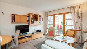 Ein modernes Wohnzimmer mit Flachbildfernseher, Holzschränken, einer Couch und einem Esstisch.