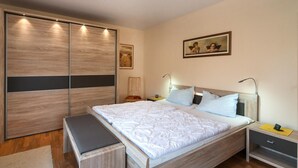 Ein Schlafzimmer mit einem großen Bett, Nachttischen, einer Bank, einem Kleiderschrank und einem Bild an der Wand.