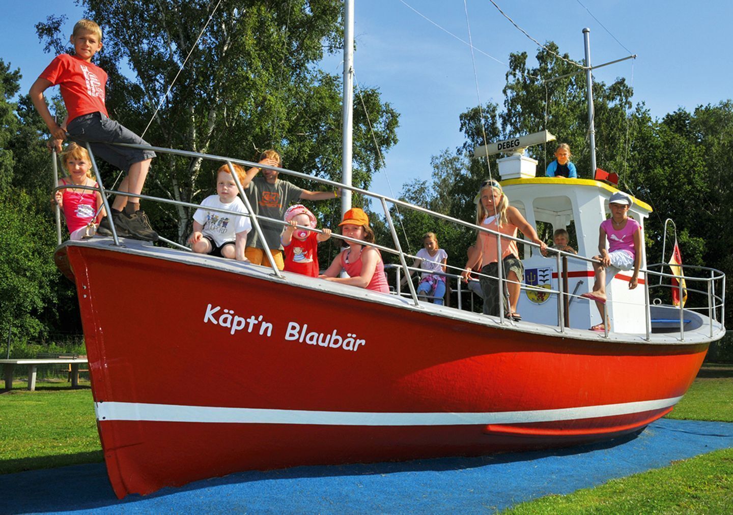 Un barco rojo con la inscripción 'Käpt'n Blaubär' en el costado, pasajeros en la cubierta y una bandera.