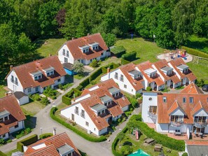 Un quartier résidentiel composé de plusieurs maisons aux toits recouverts de tuiles rouges et aux murs blancs, le tout entouré d’une végétation luxuriante.