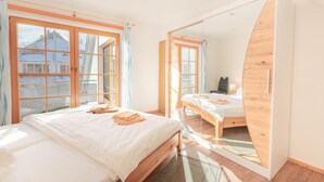 A bedroom with a large mirror, wooden bed frame, and a view of a building through the window. - Spacious vacation apartment with balcony and pool in the Freesenbruch Zingst vacation park - (Zingst)