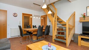A modern living room with a wooden staircase, a dining area with a table and chairs, and a TV stand. - Spacious vacation apartment with balcony and pool in the Freesenbruch Zingst vacation park - (Zingst)