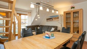A modern dining area with a wooden table, black chairs, and a ceiling light fixture. - Spacious vacation apartment with balcony and pool in the Freesenbruch Zingst vacation park - (Zingst)