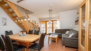 A modern living room with a wooden staircase, a dining area with a wooden table and chairs, and a grey sofa. - Spacious vacation apartment with balcony and pool in the Freesenbruch Zingst vacation park - (Zingst)