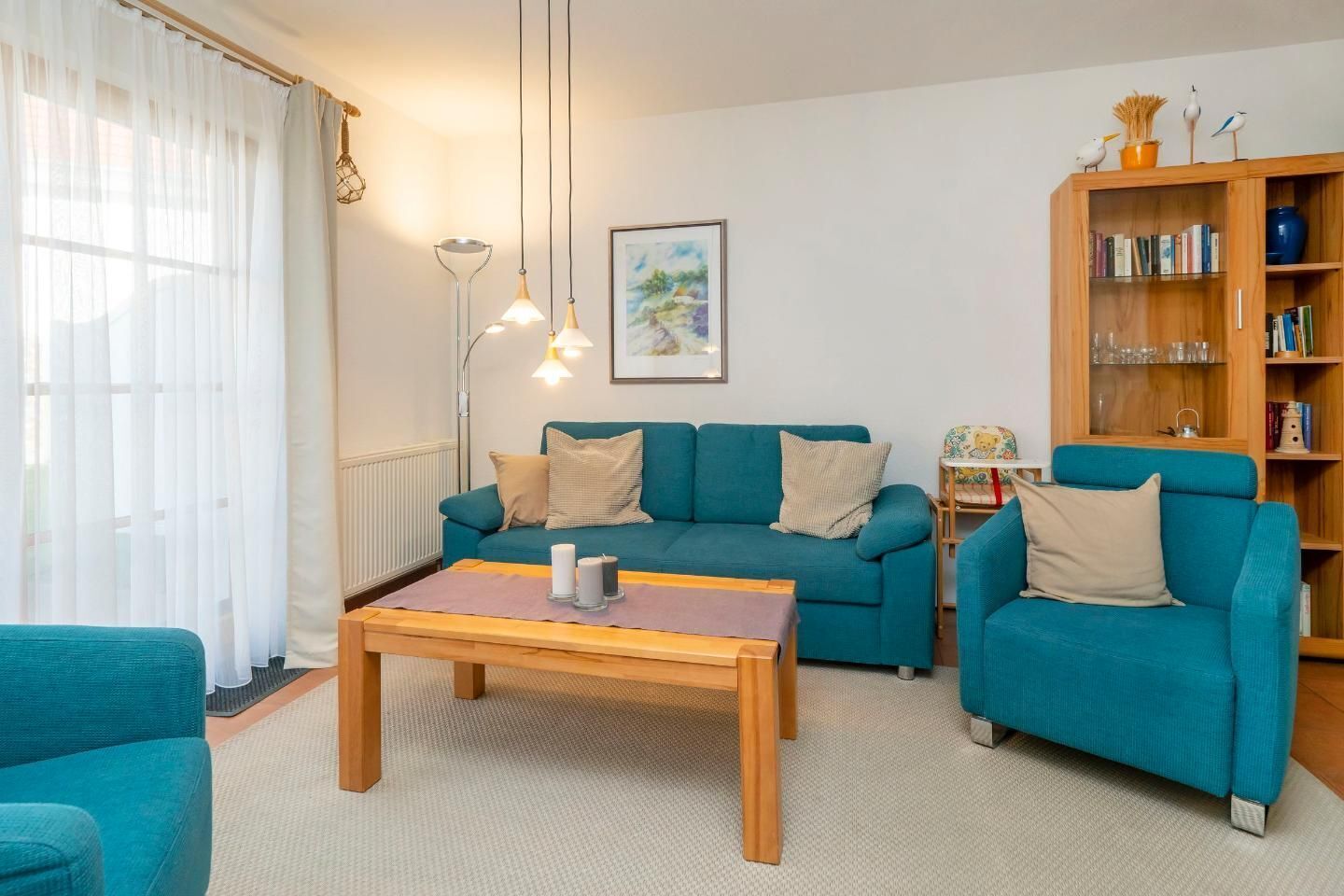 Ein Wohnzimmer mit einem petrolfarbenen Sofa, einem Holztisch und einem Bücherregal.