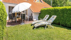 A house with a tiled roof, a patio with a table and chairs, and two lounge chairs. - Terraced house Seehund in the Freesenbruch vacation park: comfort for families in Zingst - (Zingst)
