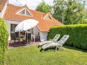 A house with a tiled roof, a patio with a table and chairs, and two lounge chairs. - Terraced house Seehund in the Freesenbruch vacation park: comfort for families in Zingst - (Zingst)