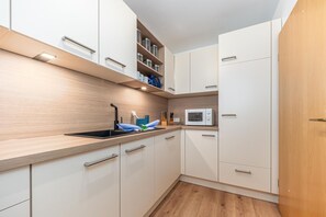 Een kleine keuken met witte kastjes, een magnetron en een spoelbak.