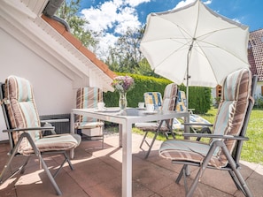 Een terras buiten met een witte tafel, vier gestreepte stoelen en een grote witte parasol.