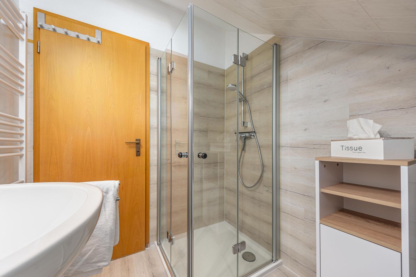 Une salle de bain moderne avec une douche à parois de verre, une porte en bois et un lavabo blanc.