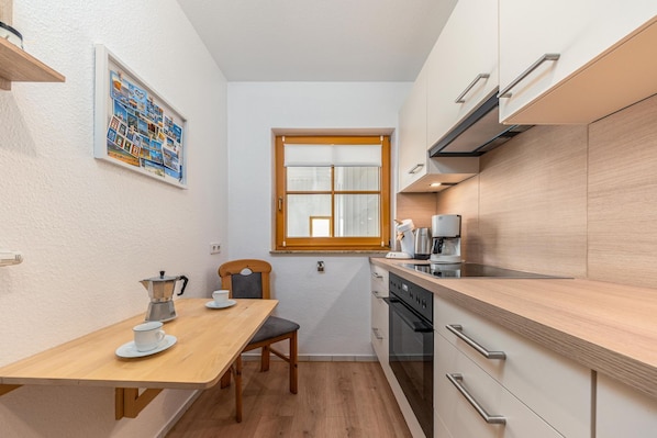 A compact kitchen with a wooden table, a coffee machine, and a window.