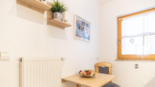 A small kitchen with a wooden table, a chair, a radiator, a window, and a wall-mounted shelf with a plant. - Terraced house Seehund in the Freesenbruch vacation park: comfort for families in Zingst - (Zingst)