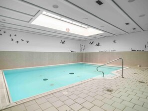 Une piscine intérieure avec un sol carrelé, une rambarde et des peintures murales représentant des oiseaux et des roseaux.
