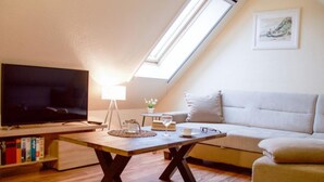 Una sala de estar acogedora con televisor de pantalla plana, una mesa de centro de madera, un sofá y un tragaluz.