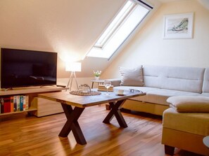 Ein gemütliches Wohnzimmer mit Fernseher, Couch, Couchtisch und Dachfenster.