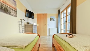 Habitación de hotel con dos camas, televisión, radiador y ventana con cortinas.