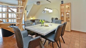 Un comedor con una mesa grande, seis sillas y una lámpara de araña moderna. Se ve una escalera de madera al fondo.