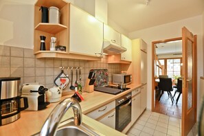 Eine moderne Küche mit Herd, Mikrowelle und Spüle. Durch eine offene Tür ist ein Essbereich mit Tisch und Stühlen zu sehen.