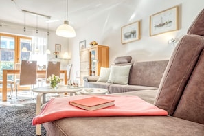 Uma sala de estar moderna com um sofá marrom, uma mesa de jantar com cadeiras e uma cozinha ao fundo.