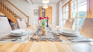 A dining area with a wooden table set for four, surrounded by chairs. There are candles, a vase with flowers, and a decorative runner on the table. - Comfortable terraced house in a vacation park with terrace and garden in Zingst - (Zingst)