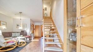 A modern living room with a curved staircase, a sofa set, and a glass cabinet with glasses. - Comfortable terraced house in a vacation park with terrace and garden in Zingst - (Zingst)