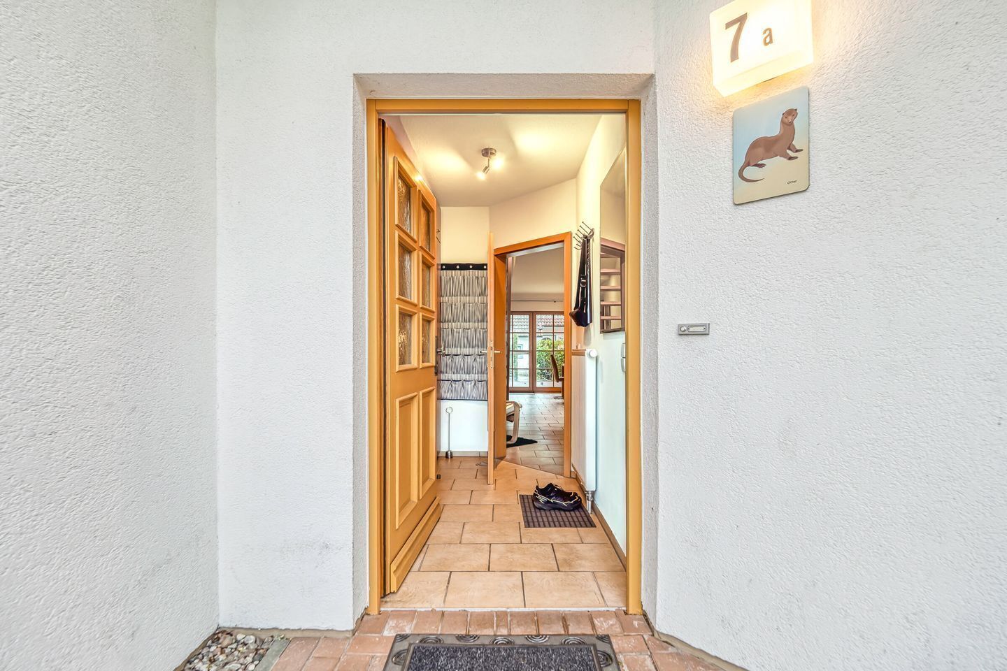 A hallway with a wooden door, a tiled floor, and a small rug at the entrance.