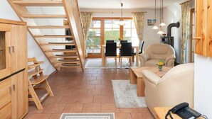 A modern living room with a wooden staircase, a dining area, and a sofa. - Terraced house in Zingst with terrace, garden view and heated indoor pool - (Zingst)