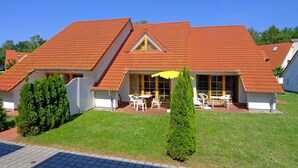 A two-story house with a red-tiled roof, a covered patio with outdoor furniture, and a well-maintained lawn. - Terraced house in Zingst with terrace, garden view and heated indoor pool - (Zingst)