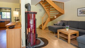 A living room with a wood-burning stove, a sofa, a coffee table, and a staircase. - Comfortable semi-detached house with sauna, garden and terrace in the Zingst vacation park (Zingst)