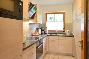 Cocina compacta con microondas, estufa, fregadero y ventana con vistas a zonas verdes.
