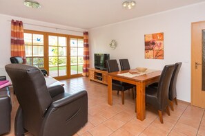 Una sala de estar con sofá, una mesa de comedor con sillas, un televisor y una ventana con cortinas.