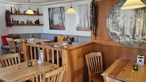 Ein gemütliches Restaurant-Interieur mit Holztischen und -stühlen, Pendelleuchten und Waldbildern an den Wänden.
