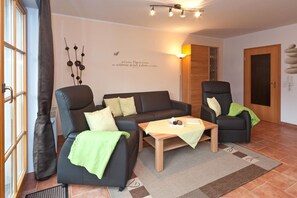 A living room with a sofa, two armchairs, a coffee table, and a wall with a decorative item.